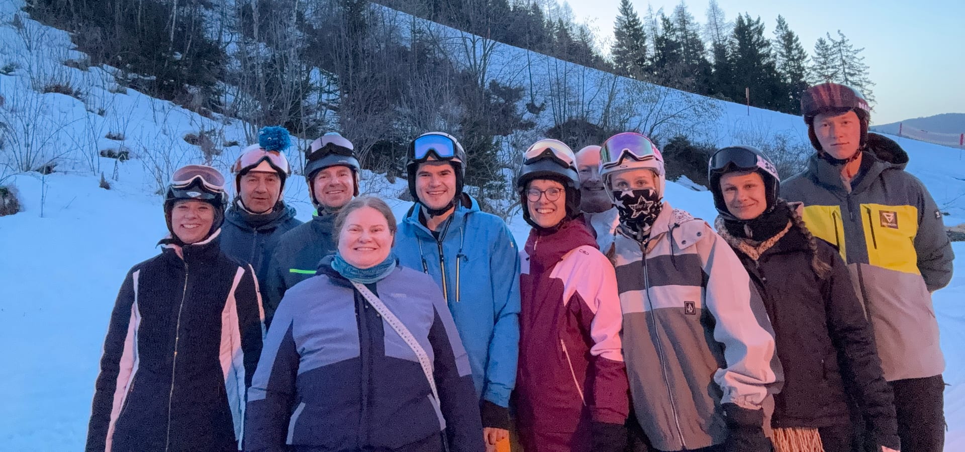 Gruppenfoto der Teilnehmenden in Skikleidung und mit Helmen am Pistenrand im Abendlicht